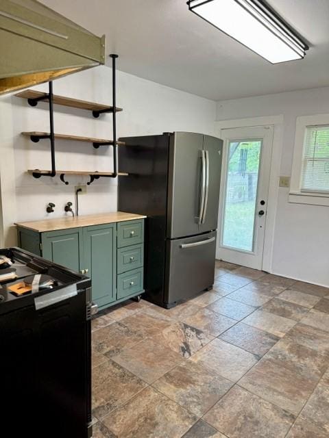 kitchen featuring green cabinetry, open shelves, stone finish flooring, freestanding refrigerator, and electric stove