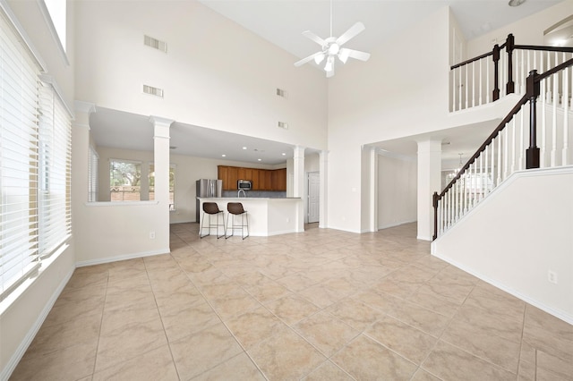 unfurnished living room featuring a ceiling fan, visible vents, stairway, and ornate columns