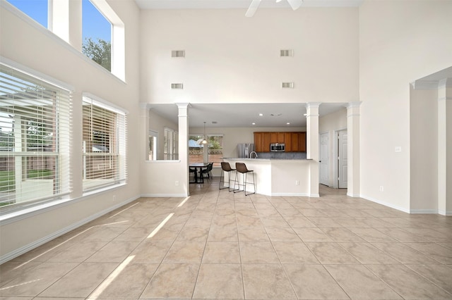 living room featuring visible vents, decorative columns, light tile patterned flooring, and a towering ceiling