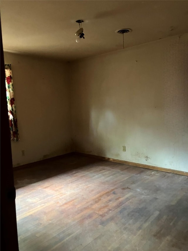 unfurnished room with baseboards, wood finished floors, and visible vents