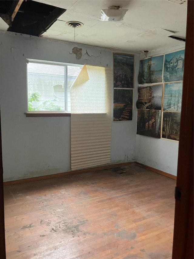 empty room featuring wood-type flooring, baseboards, and visible vents