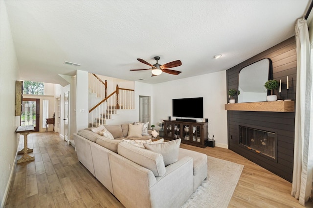 4406 Tarlton Way, Sugar Land, TX 77478 - living area featuring light wood-style floors, a glass covered fireplace, stairway, ceiling fan, and a textured ceiling