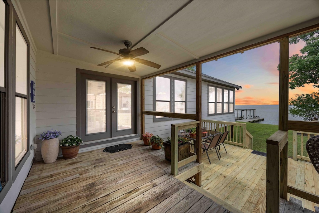 deck at dusk with outdoor dining space, ceiling fan, a water view, and french doors