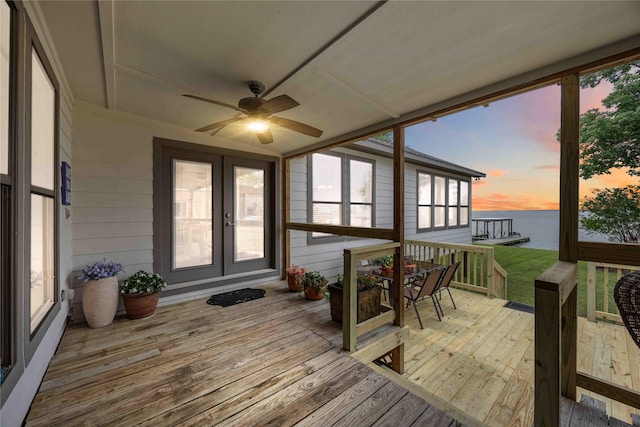 deck at dusk with outdoor dining space, ceiling fan, a water view, and french doors