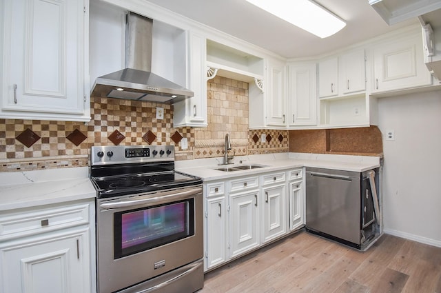kitchen with a sink, stainless steel appliances, light wood-type flooring, wall chimney range hood, and white cabinets