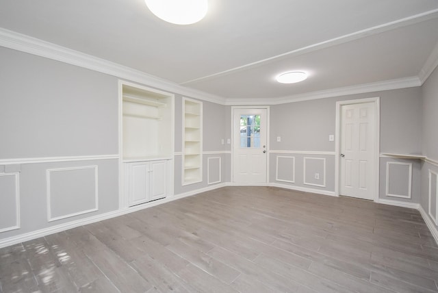 spare room featuring wood finished floors, ornamental molding, built in features, and wainscoting