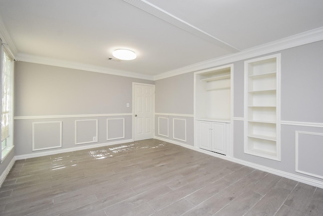 spare room with visible vents, wood finished floors, built in shelves, and ornamental molding