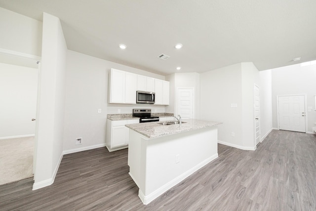 8113 Burnt Orchid Dr, Houston, TX 77016 - kitchen with stainless steel appliances, a center island with sink, wood finished floors, white cabinets, and recessed lighting