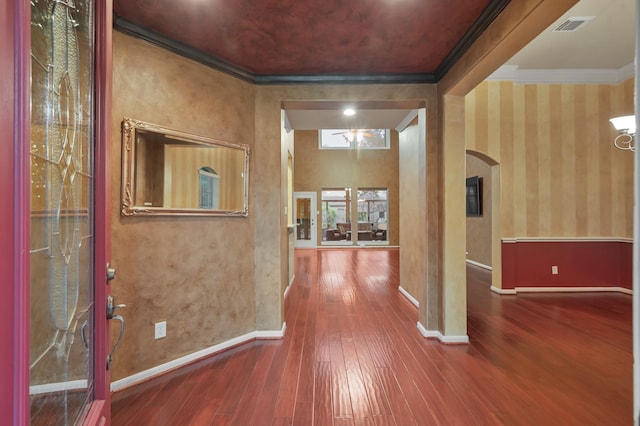 hallway featuring wood-type flooring, arched walkways, baseboards, and ornamental molding