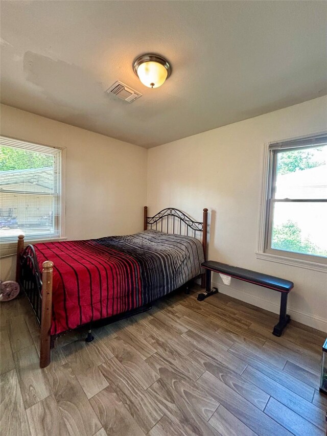 bedroom with baseboards, visible vents, wood finished floors, and multiple windows