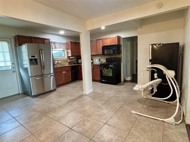 kitchen featuring decorative backsplash, brown cabinetry, light tile patterned floors, black appliances, and dark countertops