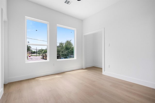empty room featuring visible vents, light wood-type flooring, and baseboards