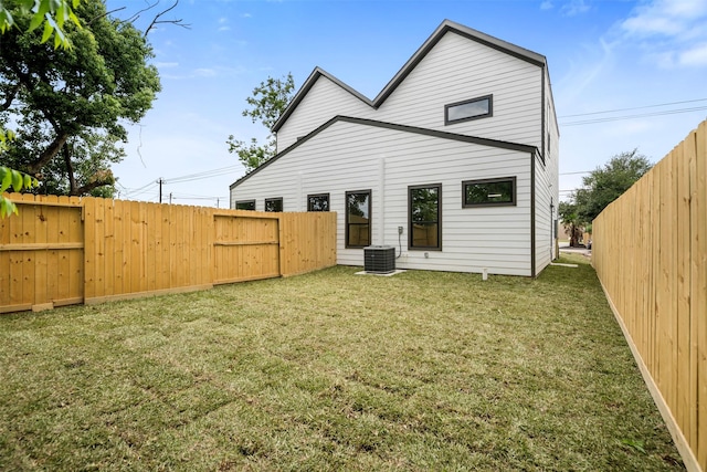 rear view of house featuring a lawn, central air condition unit, and a fenced backyard