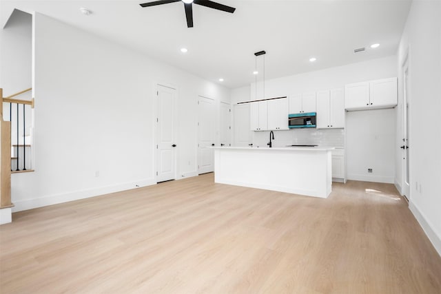 kitchen with white cabinets, a ceiling fan, light wood-style floors, and stainless steel microwave