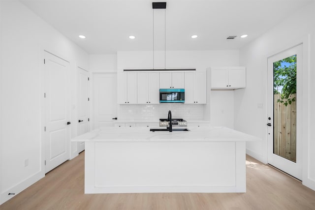 kitchen featuring tasteful backsplash, stainless steel microwave, light wood-type flooring, and white cabinetry