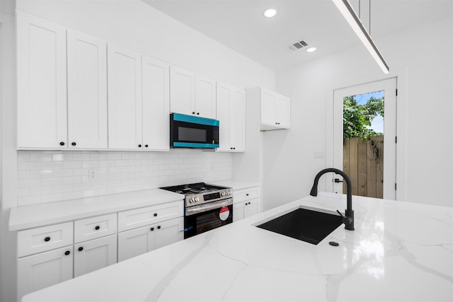 kitchen featuring decorative backsplash, white cabinets, a sink, stainless steel gas range, and light stone countertops