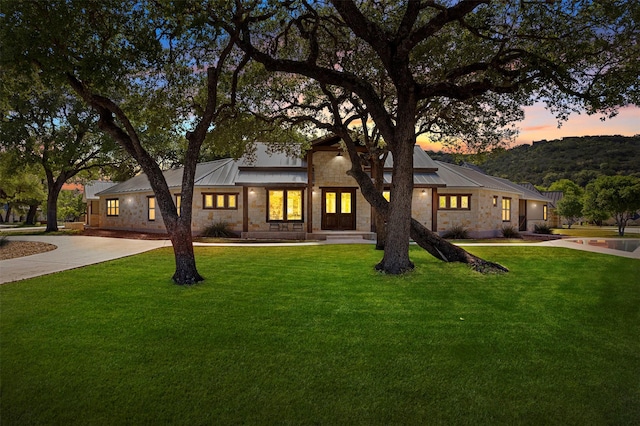 view of front of house with a front lawn, driveway, metal roof, and stone siding