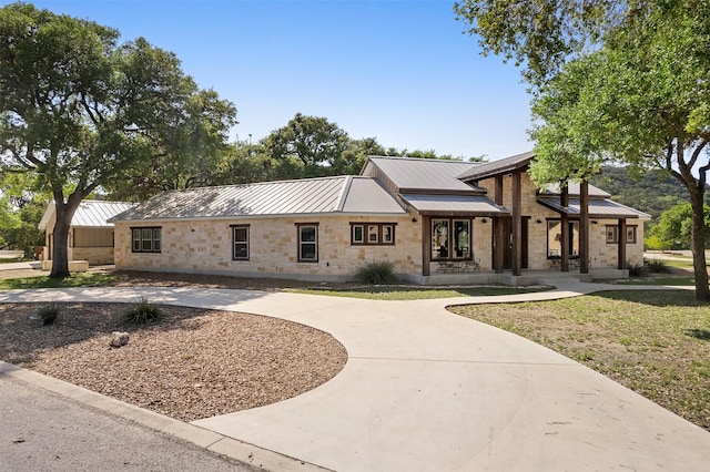 view of front of house featuring metal roof, stone siding, and curved driveway