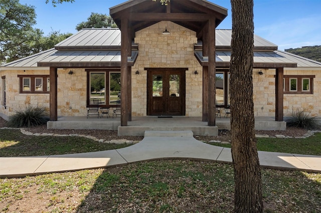 doorway to property with covered porch, a standing seam roof, metal roof, and stone siding