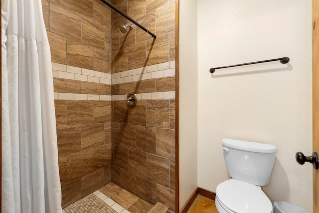 bathroom with toilet, tiled shower, and baseboards