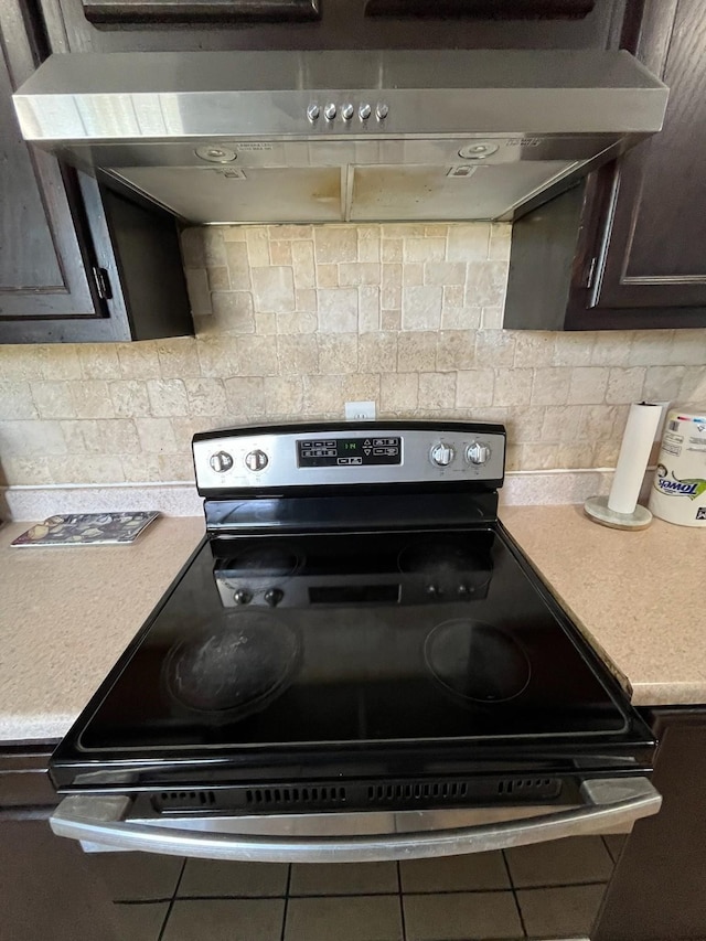 kitchen with electric stove, backsplash, under cabinet range hood, and dark brown cabinetry
