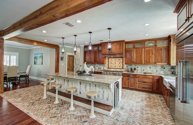 kitchen featuring visible vents, brown cabinetry, a kitchen breakfast bar, a center island, and light stone counters
