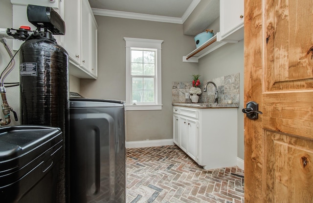 laundry area featuring crown molding, cabinet space, a sink, baseboards, and brick floor