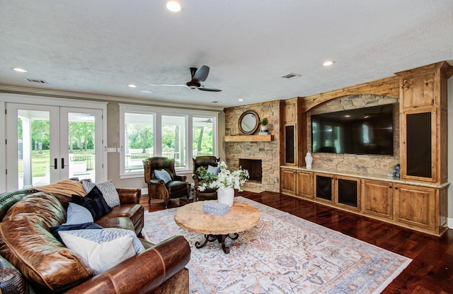 living area with dark wood-style flooring, ceiling fan, a stone fireplace, french doors, and visible vents