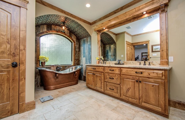 full bathroom featuring stone tile flooring, crown molding, double vanity, a soaking tub, and a sink