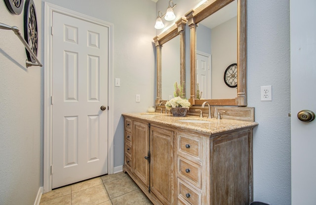 full bath featuring baseboards, double vanity, tile patterned floors, and a sink