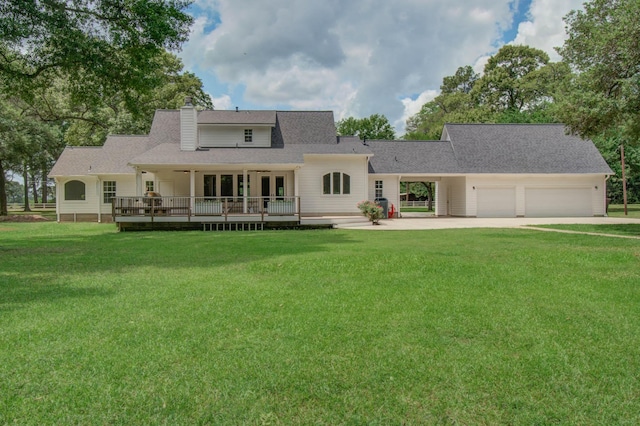 back of property with a wooden deck, driveway, a chimney, an attached garage, and a yard
