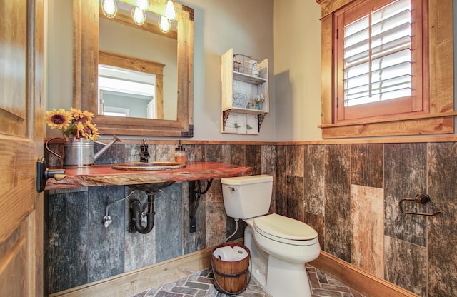bathroom featuring a sink, wainscoting, toilet, and tile walls