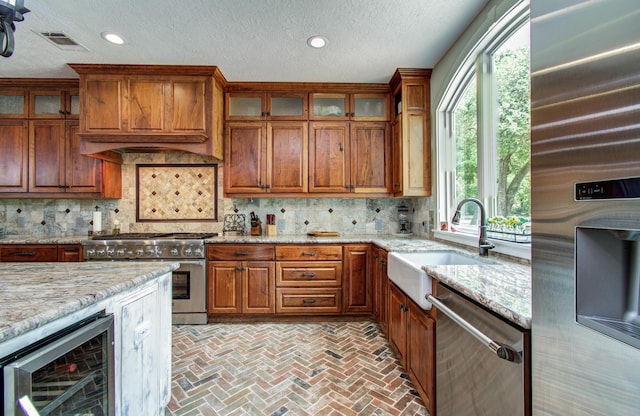 kitchen with brown cabinets, appliances with stainless steel finishes, a sink, wine cooler, and visible vents