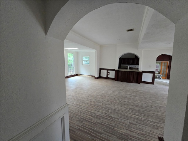 unfurnished living room featuring wood finished floors, visible vents, a textured wall, arched walkways, and baseboards