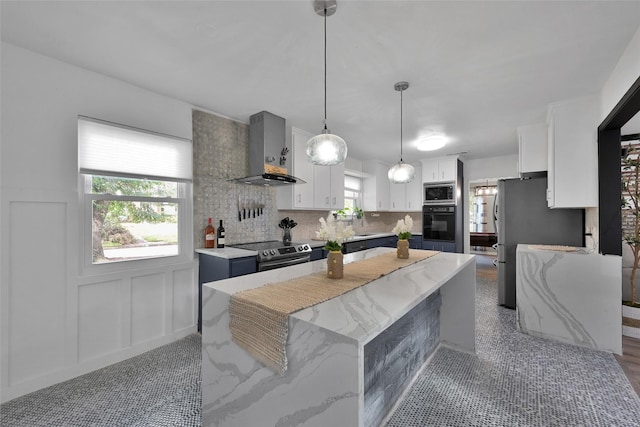 kitchen with wall chimney range hood, a kitchen island, appliances with stainless steel finishes, tasteful backsplash, and white cabinets