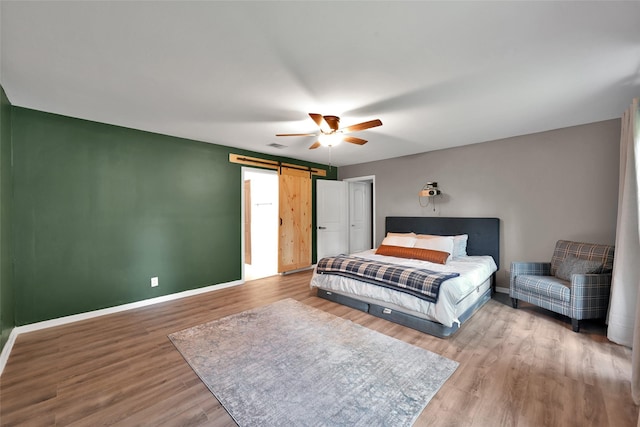 bedroom with a ceiling fan, baseboards, a barn door, and wood finished floors