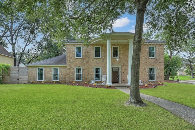 neoclassical / greek revival house with brick siding, fence, and a front yard