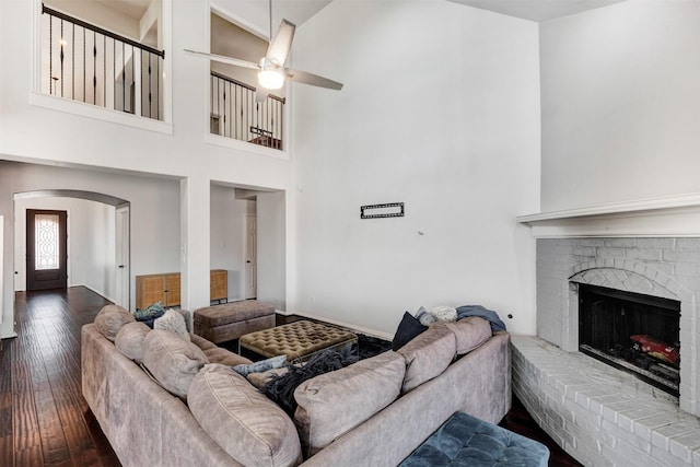 living area with arched walkways, wood-type flooring, a fireplace, a ceiling fan, and a towering ceiling