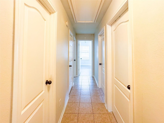corridor featuring baseboards, light tile patterned floors, and attic access