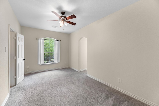 empty room with carpet floors, arched walkways, a ceiling fan, baseboards, and visible vents