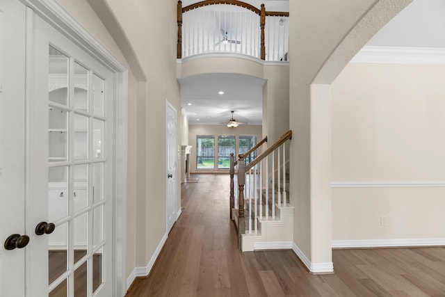 foyer with arched walkways, ceiling fan, wood finished floors, and stairway
