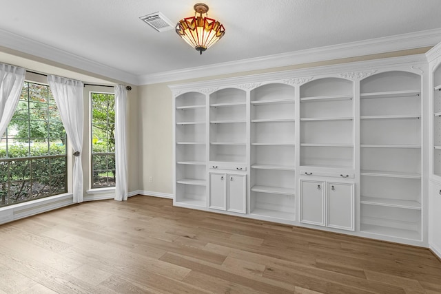 empty room with crown molding, built in shelves, baseboards, wood finished floors, and visible vents