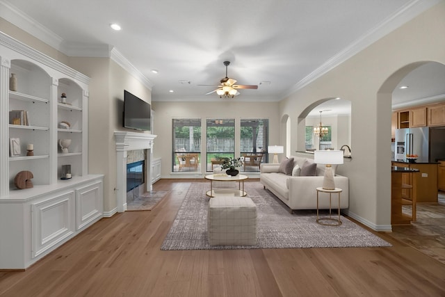 living room with light wood-style floors, plenty of natural light, ceiling fan with notable chandelier, and a premium fireplace