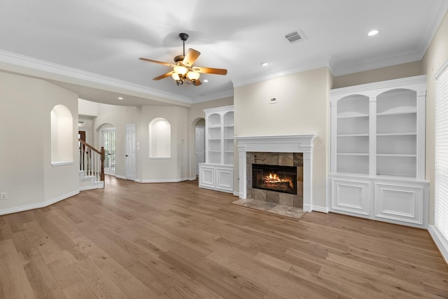 unfurnished living room with a fireplace, arched walkways, a ceiling fan, light wood-type flooring, and ornamental molding