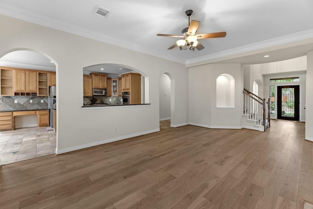 unfurnished living room featuring crown molding, ceiling fan, light wood finished floors, arched walkways, and visible vents