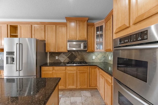kitchen featuring backsplash, a textured ceiling, appliances with stainless steel finishes, glass insert cabinets, and dark stone counters