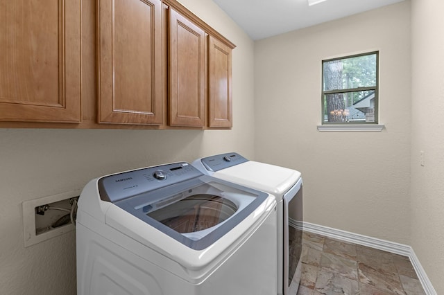 washroom with baseboards, cabinet space, washer and dryer, and stone finish floor