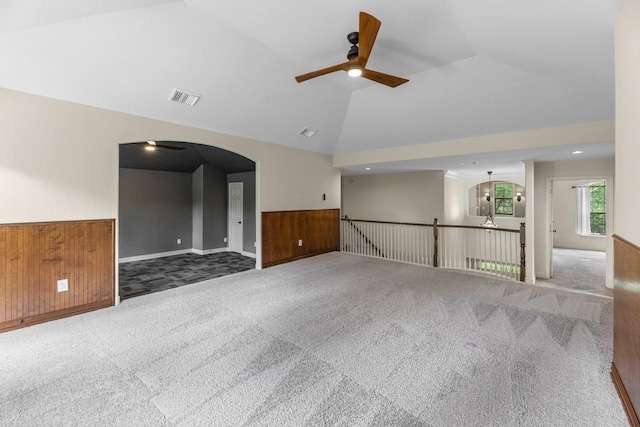 carpeted spare room with visible vents, ceiling fan, wooden walls, high vaulted ceiling, and a wainscoted wall