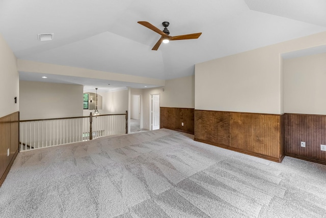 empty room with carpet flooring, ceiling fan, visible vents, a wainscoted wall, and vaulted ceiling