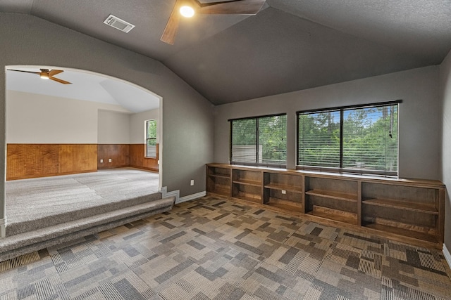 carpeted spare room featuring a ceiling fan, visible vents, arched walkways, a wainscoted wall, and lofted ceiling